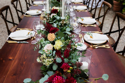 in backyard of villa in Tuscany there is banquet wooden table decorated with cotton and eucalyptus compositions, glasses.